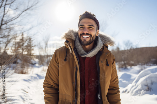 A young latin male is walking happily with in a winter coat with a winter hat in a in snow covered country landscape during day in winter on a bright and sunny day