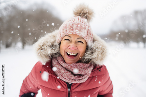 A senior caucasian woman is playing in the snow happily with a winter coat and a winter hat in a in snow covered country landscape during day in winter on a bright day