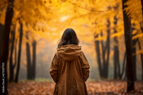 A young asian woman is posing in front of the camera from the front happily with an autumn coat in a forest during sunset in autumn with no leaves on the trees photo