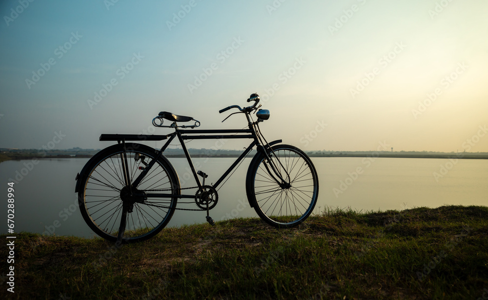 Obraz premium Old bicycle in meadow near the river during sunrise