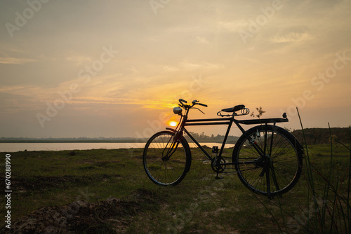Silhouete of old rusty retro style bicycle in meadow during sunrise.