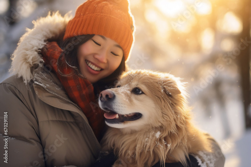 A senior asian woman is playing happily with the dog in the snow with a winter coat and winter hat in a in snow covered forest during sunset in winter while snowing