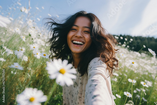 A young asian woman is is making a selfie while smiling with a profesional camera in a meadow full of daisies a low tech social media woman