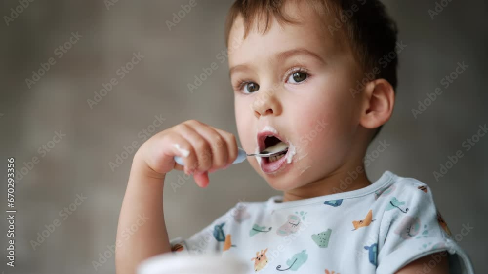 One and a half year old child eating yogurt. Kid finishes the cup and stretches it to camera. Close up. Low angle view. One and a half year old child eating yogurt. Kid finishes the cup and stretches it to camera. Close up. Low angle view.