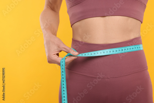 Slim woman measuring waist with tape on yellow background, closeup. Weight loss