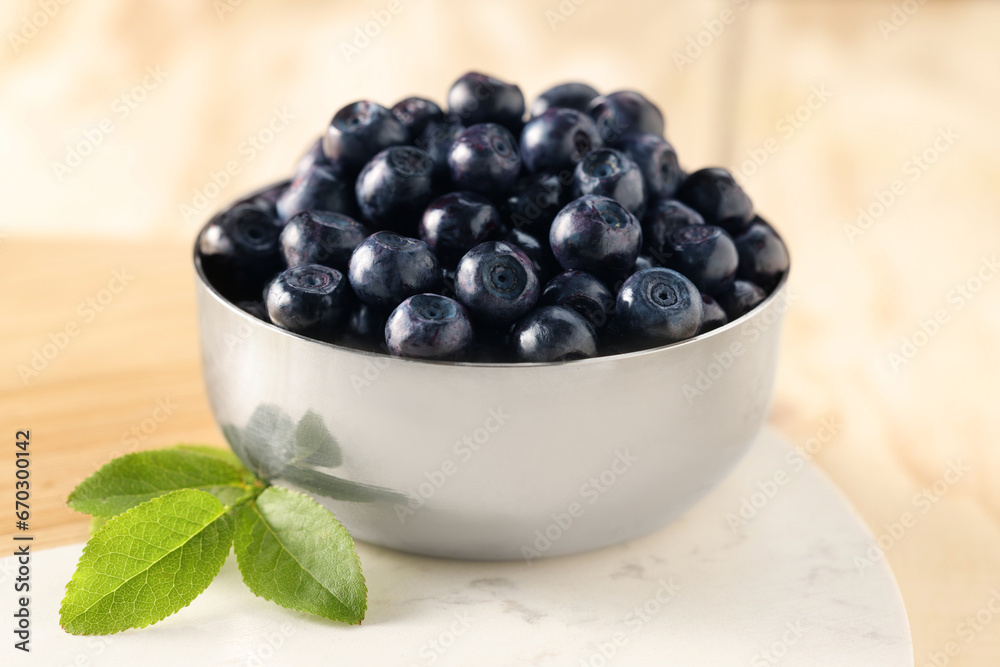 Bowl of tasty fresh bilberries and green leaves on light table, closeup Bowl of tasty fresh bilberries and green leaves on light table, closeup