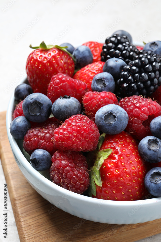 Many different fresh ripe berries in bowl on light grey table, closeup Many different fresh ripe berries in bowl on light grey table, closeup