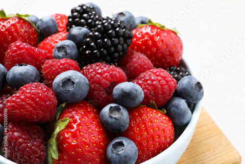 Many different fresh ripe berries in bowl on light grey table  closeup