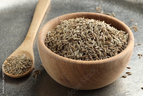 Bowl of caraway seeds and spoon on grey table, closeup photo