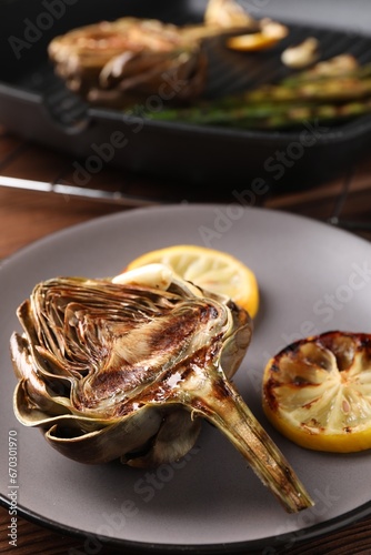 Tasty grilled artichoke and slices of lemon on table, closeup