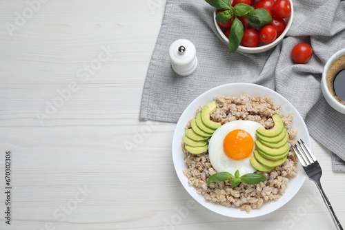 Delicious boiled oatmeal with fried egg and avocado served on white wooden table, flat lay. Space for text