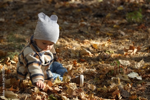 Cute little child on ground with autumn dry leaves outdoors, space for text