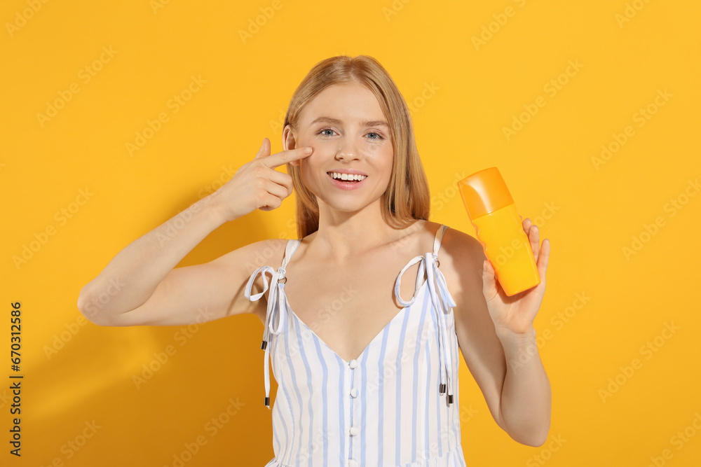 Beautiful young woman holding sun protection cream on orange background Beautiful young woman holding sun protection cream on orange background
