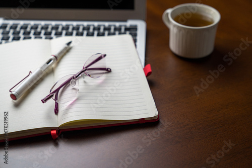 Eyeglasses on top of notepad and computer laptop and next to a cup of tea. Copy space.