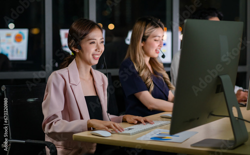 Asian professional successful female businesswomen assistant night shift call center helpline in formal business outfit and microphone headphones sitting smiling talking helping customers online