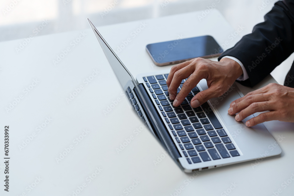Close up. Asian businessman working with laptop computer at modern office Businessman in black suit working and typing on laptop keyboard Internet online at the desk in the office.