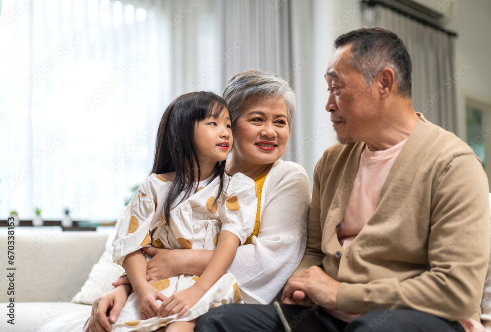 Fototapeta premium Portrait of happy love asian grandfather with grandmother and asian little cute girl enjoy relax at home.Young girl with their laughing grandparents smiling together.Family and togetherness