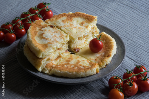 Homemade cheese filled savoury pies khachapury on grey plate served with tomatoes. Selective focus
