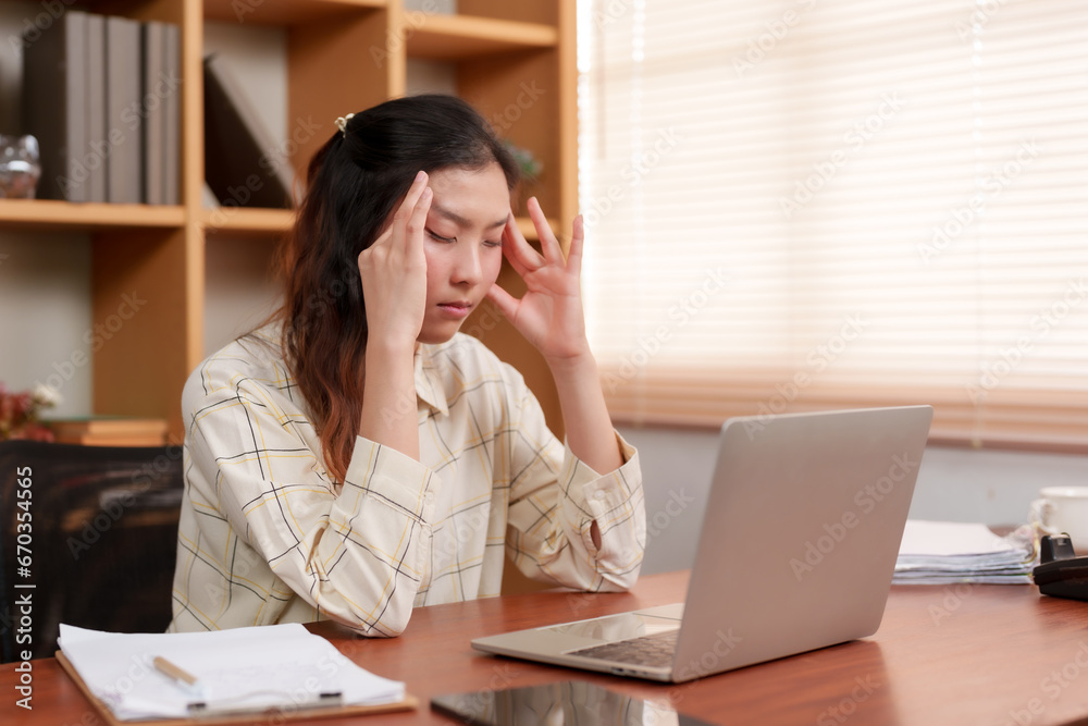 asian woman An office worker is using both hands to gently massage the forehead. After concentrating on working with a laptop computer With the boredom of routine work Have headache because of stress asian woman An office worker is using both hands to gently massage the forehead. After concentrating on working with a laptop computer With the boredom of routine work Have headache because of stress