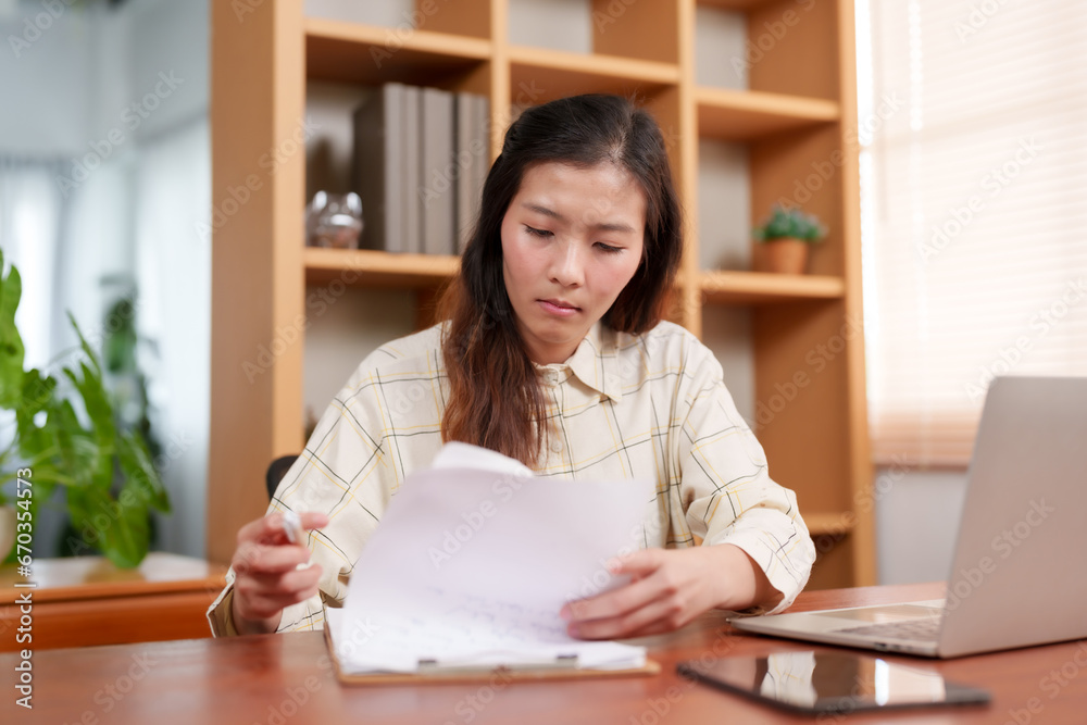 Young Asian woman, office worker, is sitting working in office, busy with work on laptop computer, signing documents that office brought for you sign, It is documented work guideline. Young Asian woman, office worker, is sitting working in office, busy with work on laptop computer, signing documents that office brought for you sign, It is documented work guideline.