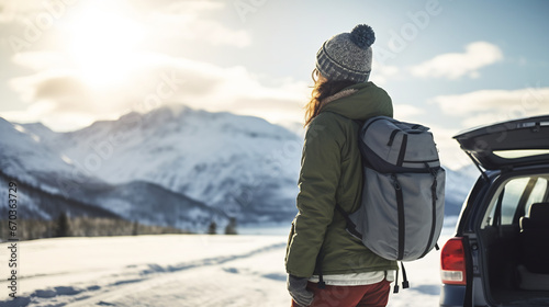 Portrait of happy traveling young woman standing near the car enjoying the view of snow mountain landscape, winter vacation outdoors