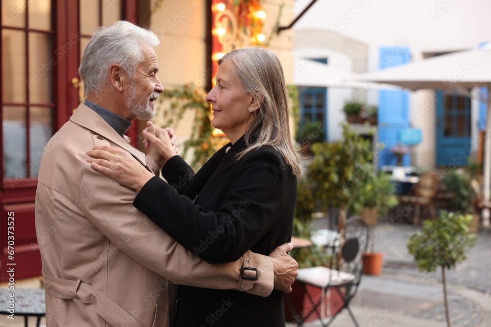 Affectionate senior couple dancing together on city street, space for text