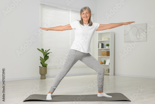 Happy senior woman practicing yoga on mat at home