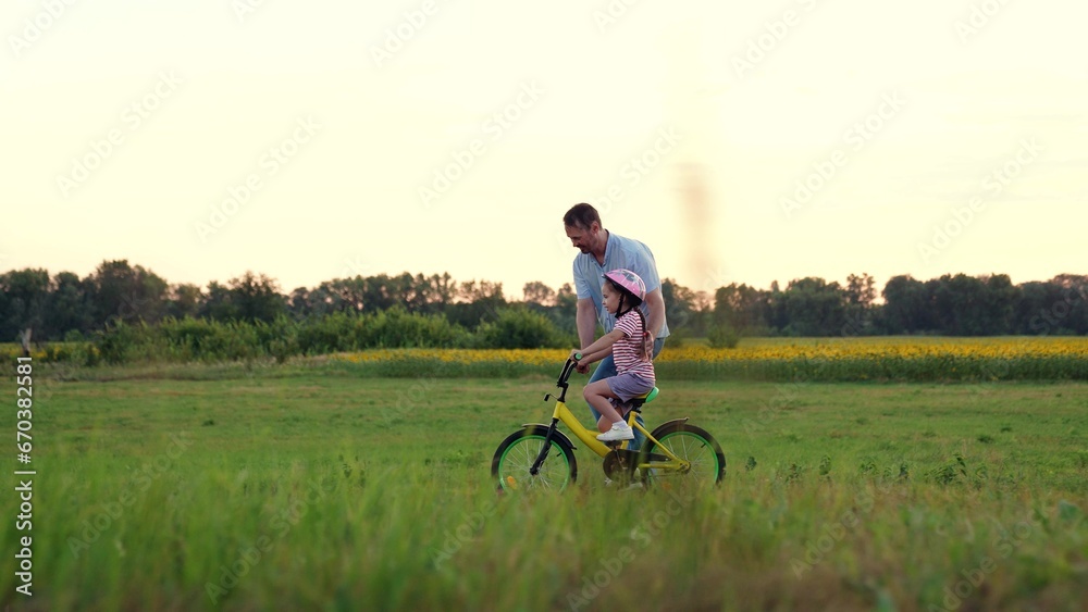 Loving father runs supporting little girl riding bicycle in summer field