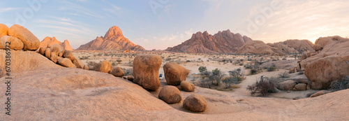 Panoramic, desert landscape of famous rounded red, granite rocks of Spitzkoppe area in early sunrise against blue sky. Picturesque rocky desert photo in calm morning in Spitzkoppe, Namibia. © minoandriani
