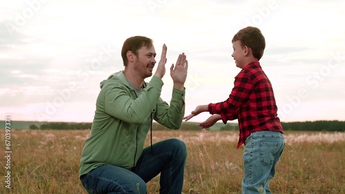 Cheerful son gives high-five to father in field with landscape view of nature beauty