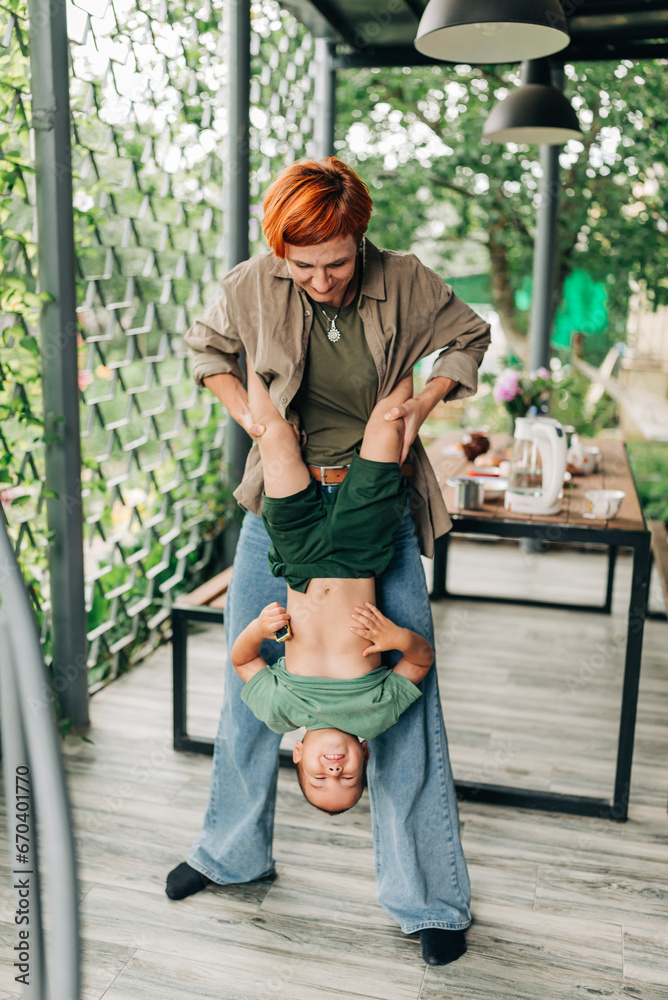 Family mother with her son holding on her hands playful mommy love enjoy time at the terrace redhead woman with short haircut Family mother with her son holding on her hands playful mommy love enjoy time at the terrace redhead woman with short haircut