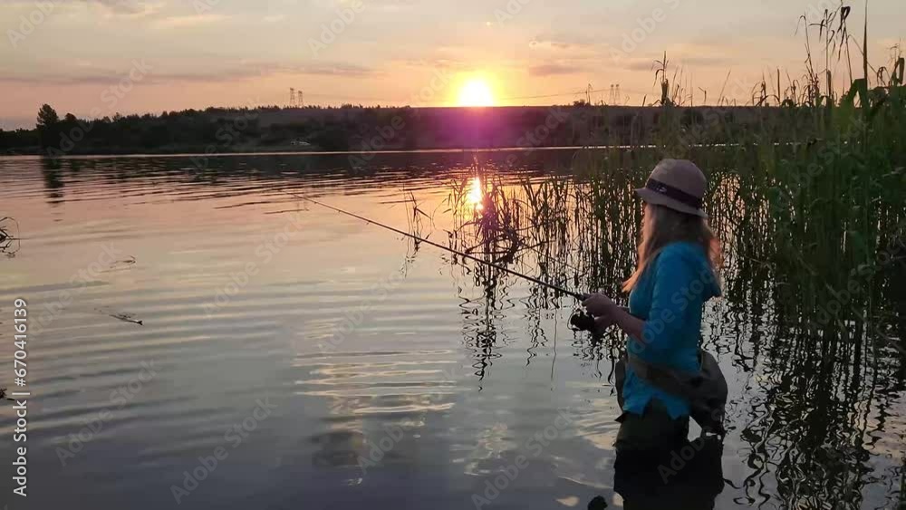A woman fishing and wading in a tranquil lake with a stunning sunset in the background A woman fishing and wading in a tranquil lake with a stunning sunset in the background