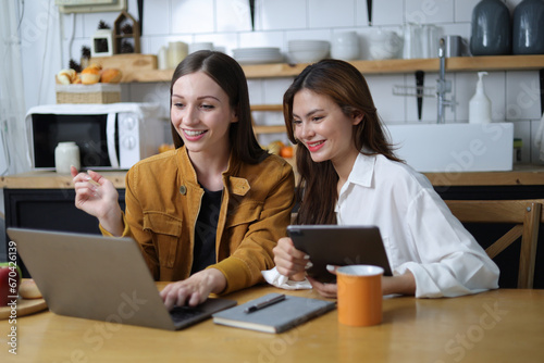 Two female students are happy while working on laptop and reading tutorial materials in home.