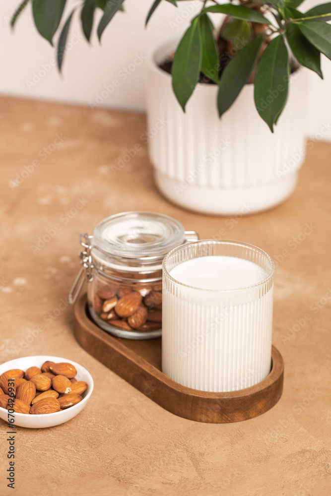 Organic almond milk in glass near the bowl with raw almonds on the table in the kitchen ready for cooking Organic almond milk in glass near the bowl with raw almonds on the table in the kitchen ready for cooking