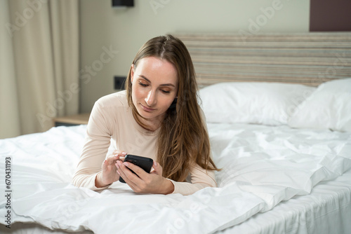 The woman is addicted to the phone, lying in bed using a smartphone. A woman is lying in bed, flipping through social networks. 