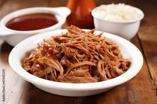 white plate with a mound of pulled pork, side cup of sauce