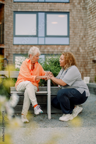 Wallpaper Mural Full length of female nurse squatting while talking to retired senior woman sitting on bench at back yard Torontodigital.ca