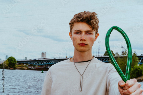 Portrait of confident man holding garden hose near river against sky photo