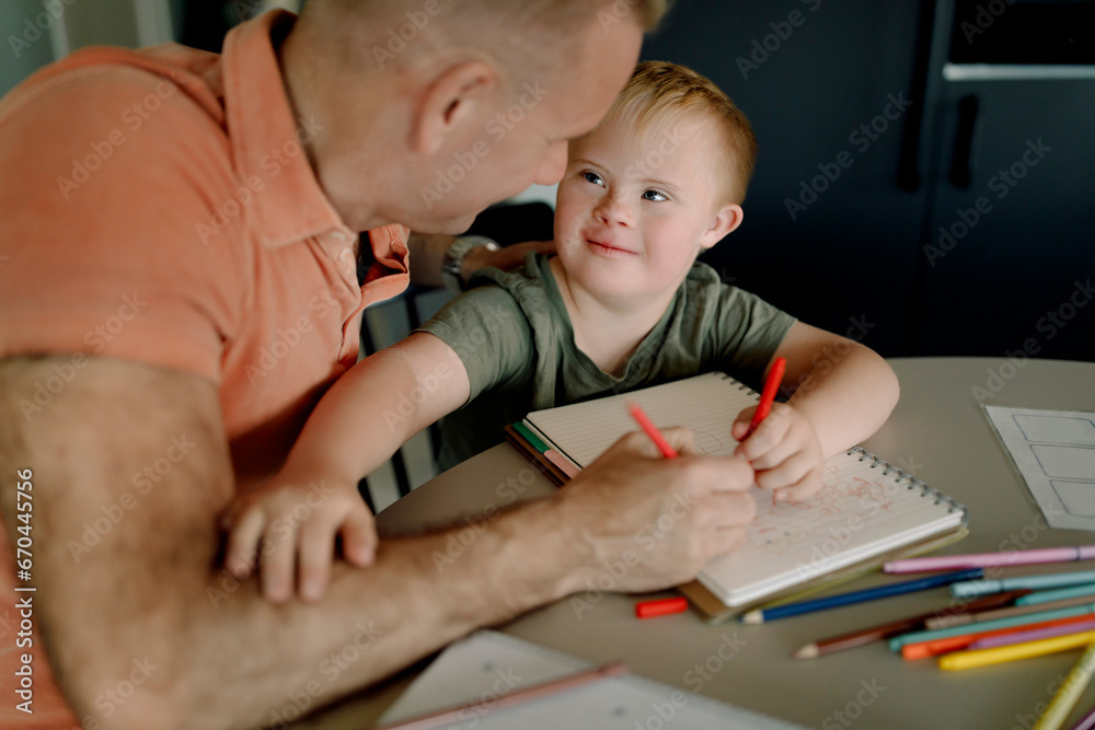 Boy with down syndrome looking at father while drawing on book