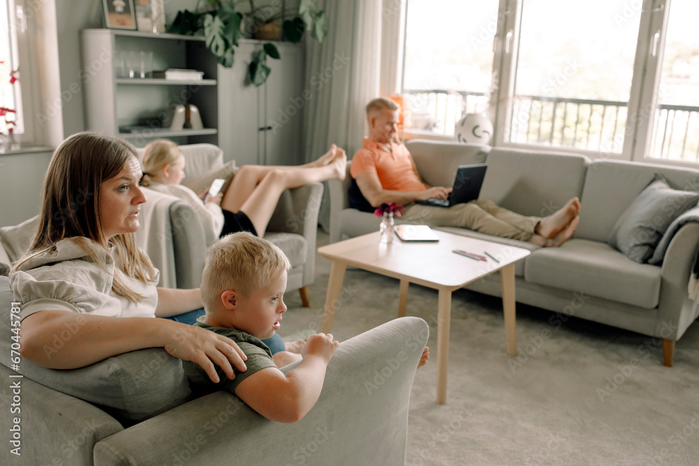 Mother and son with down syndrome watching TV while man and daughter sitting in living room at home Mother and son with down syndrome watching TV while man and daughter sitting in living room at home