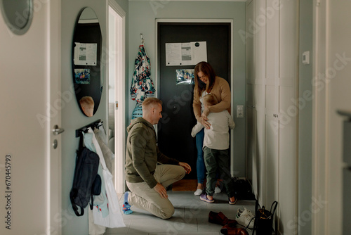 Boy embracing mother by father kneeling in mudroom at home photo