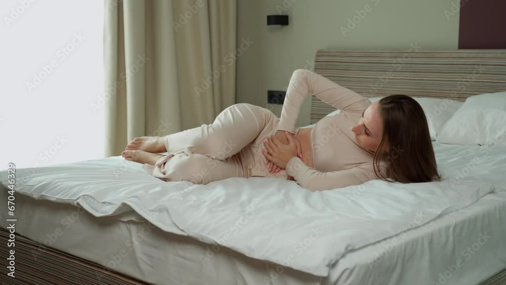 The woman has a stomach ache. The woman is lying on the bed, sick, her stomach hurts. Stomach pain