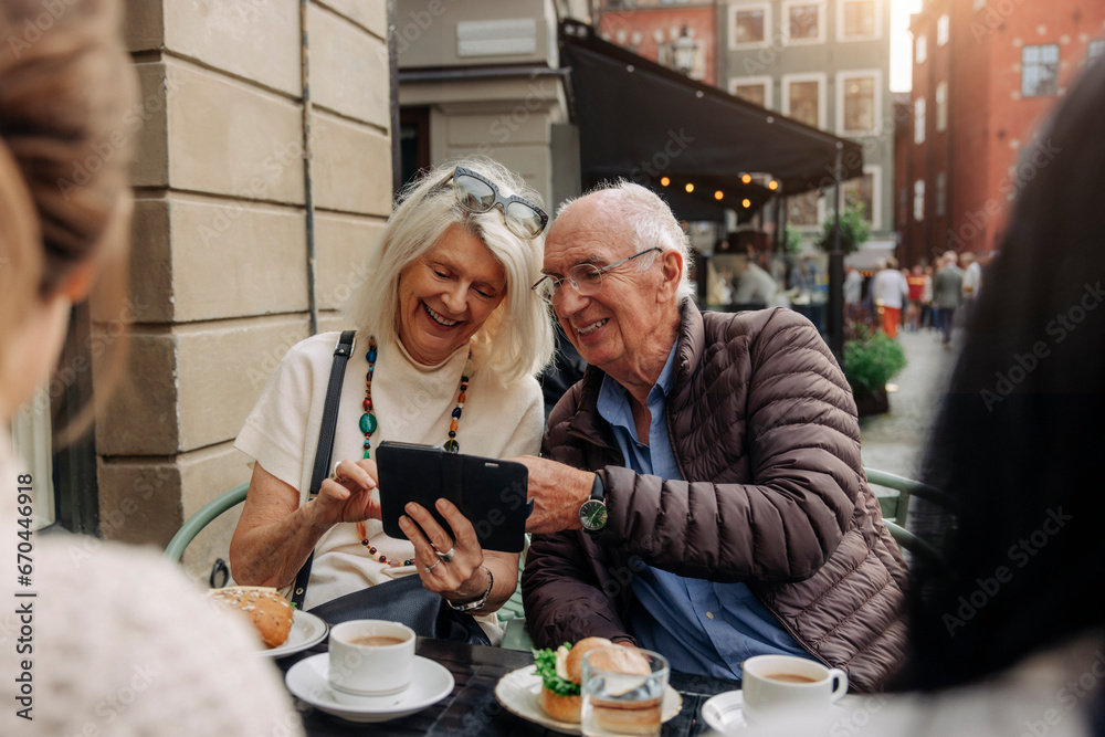 Happy senior couple sharing smart phone while sitting at sidewalk cafe