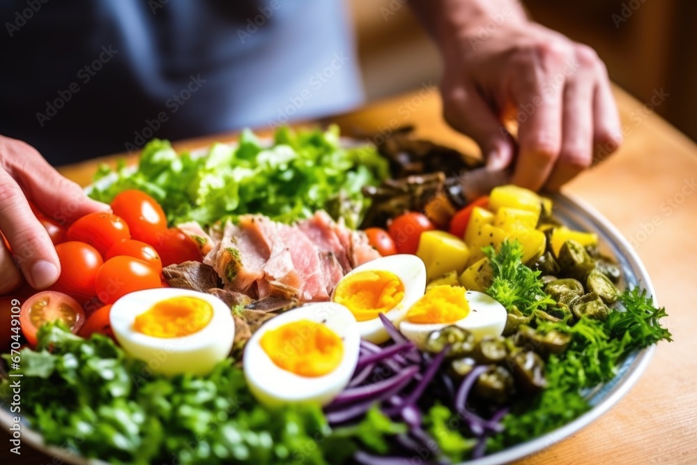 a hand delicately placing a vegetable on nicoise salad