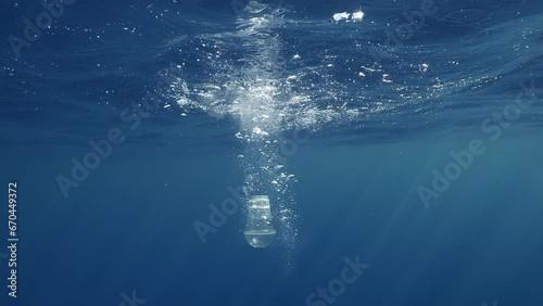 Discarded disposable plastic cocktail glass falls in water with air bubbles and floats under surface of blue water in Mediterranean Sea, Slow motion, Close-up 