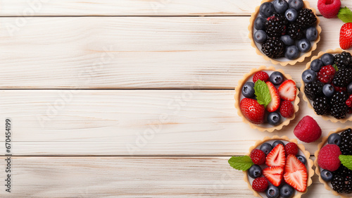 Tartlets with different fresh berries and strawberry on light wooden table space for text background 16-9