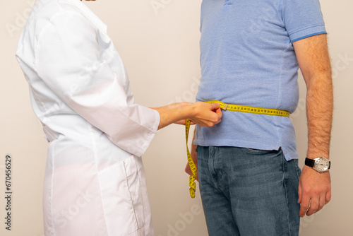 Nutritionist measuring overweight man's waist with tape in clinic, closeup