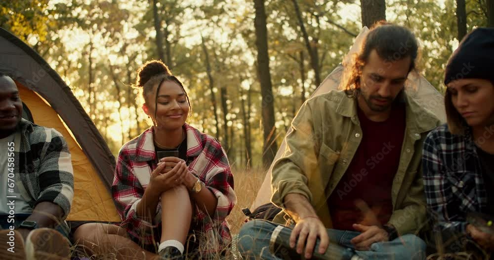 Close-up shot of a happy group of people on a hike in plaid shirts and hiking clothes pouring tea into glasses against the backdrop of a sunny summer forest. Using a thermos during a halt against the Close-up shot of a happy group of people on a hike in plaid shirts and hiking clothes pouring tea into glasses against the backdrop of a sunny summer forest. Using a thermos during a halt against the