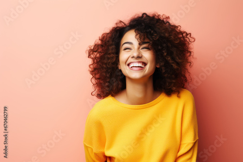 Beautiful young smiling brunette woman in a yellow sweater on a pink background