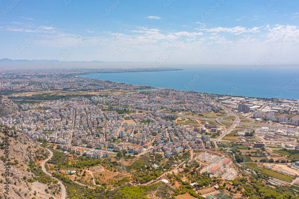 Obraz premium Flight over ridge mountain pass rocky terrain with bushes, bird's eye view overlooking the city, houses and buildings, roads and ships, Mediterranean coast, resort area, vacation trip.